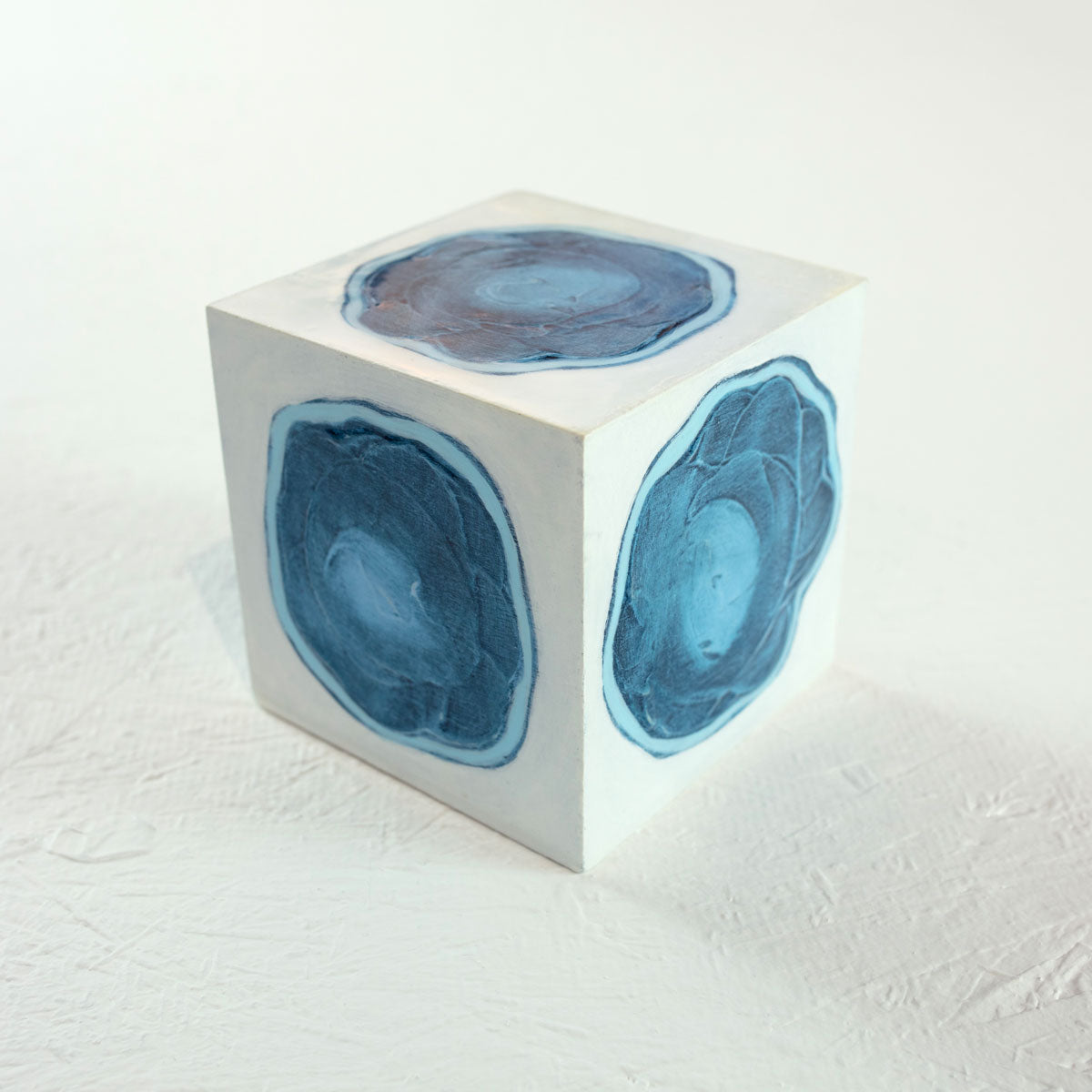 A white cube with a painted blue circle on each face rests on a white surface.