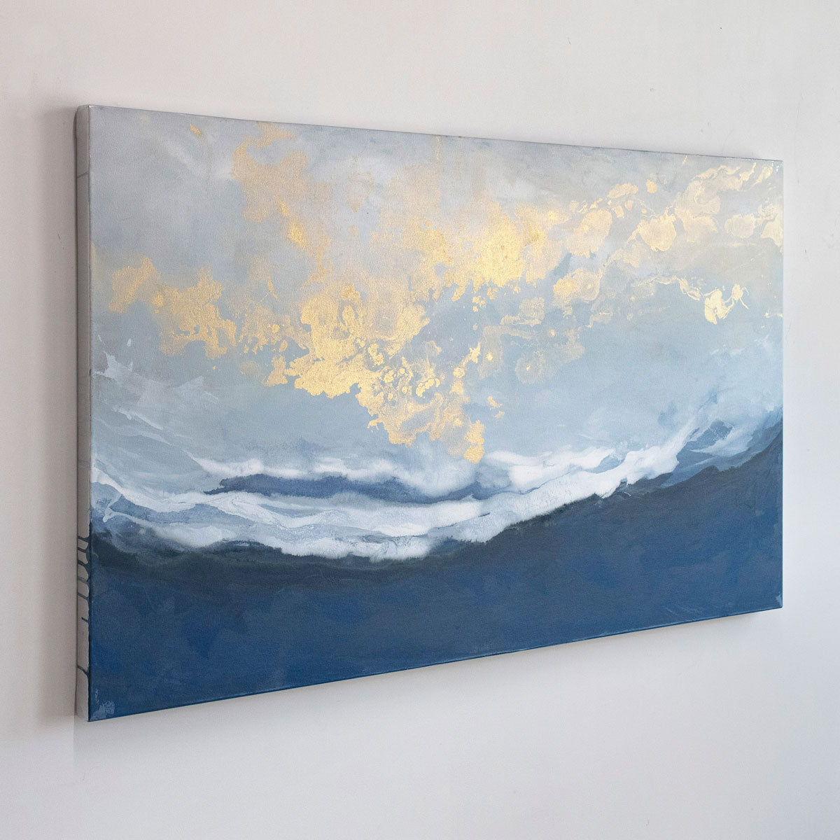 A blue, white, and gold abstract painting hangs on a light wall.
