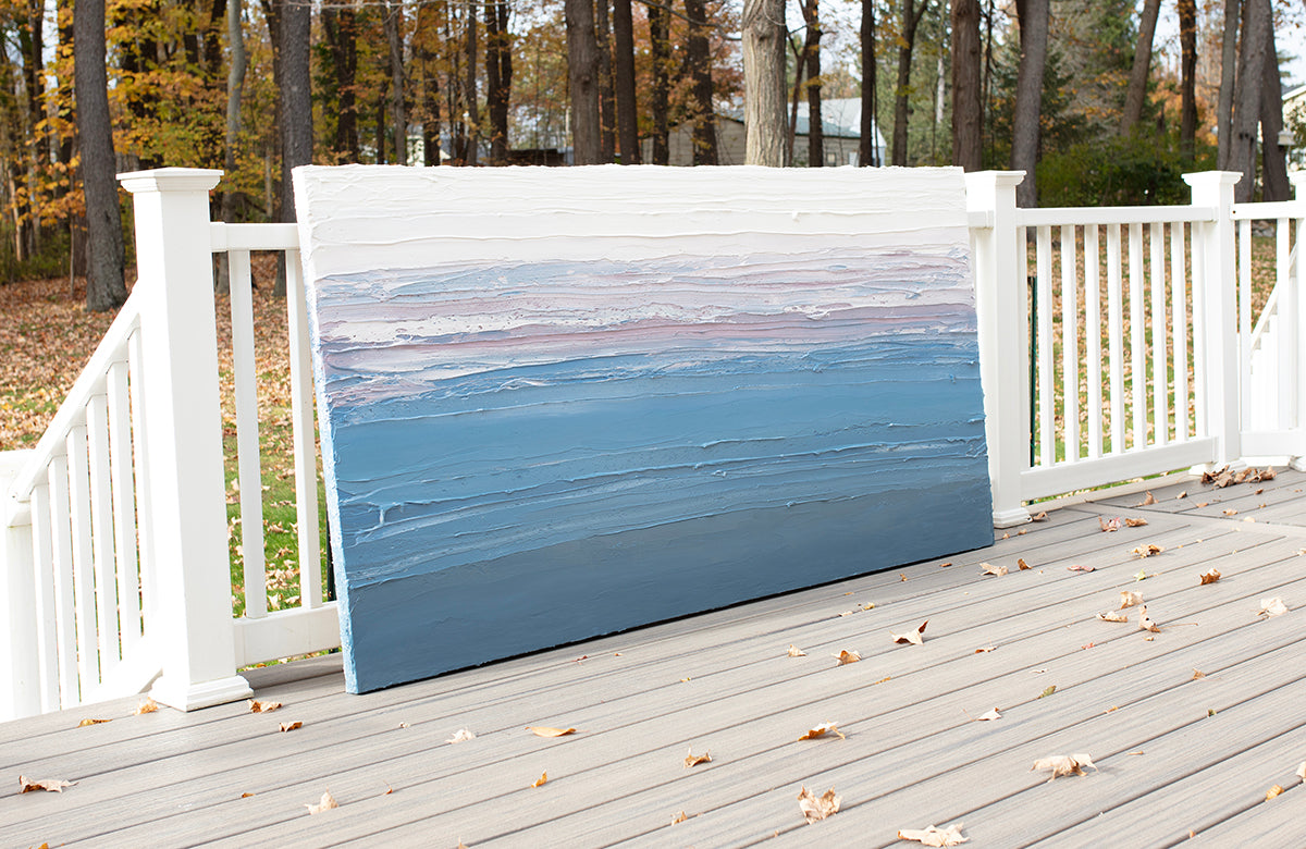 A blue, lavender and white thickly textured original abstract painting leaning on a deck outside in natural light by Teodora Guererra.