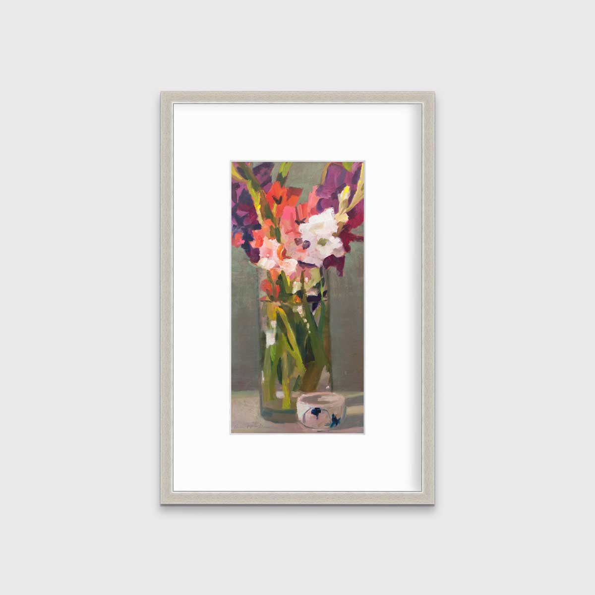 A purple, pink and green abstract floral print in a silver frame with a mat hangs on a white wall.