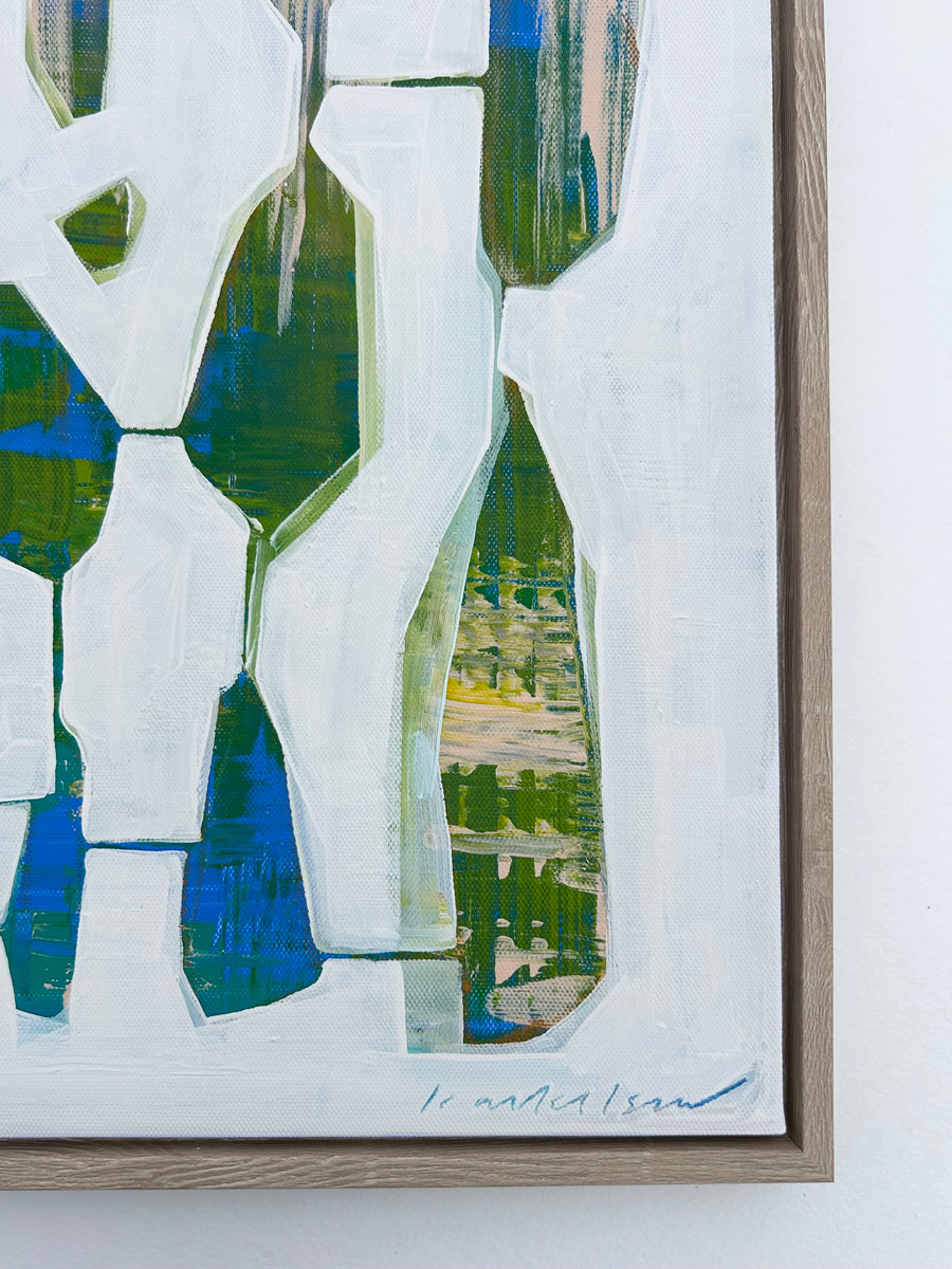 An abstract painting framed in a wood frame hangs on a white wall.