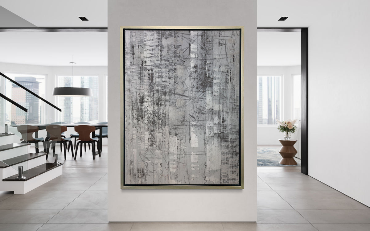 An abstract silver-grey limited edition art print by Ned Martin in a silver frame hangs on a white wall in a bright modern urban apartment.