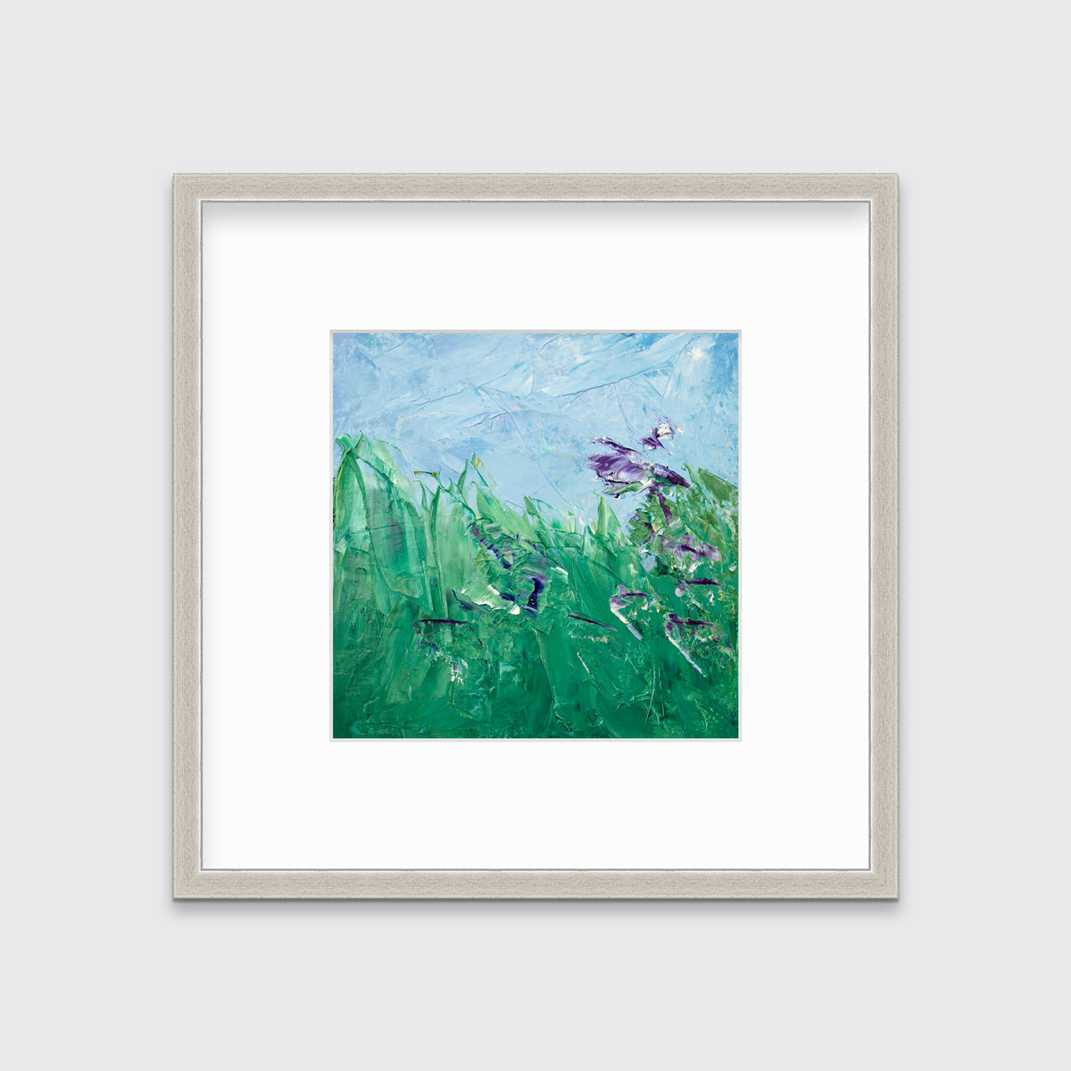 A blue, green and purple abstract landscape print in a silver frame with a mat hangs on a white wall.