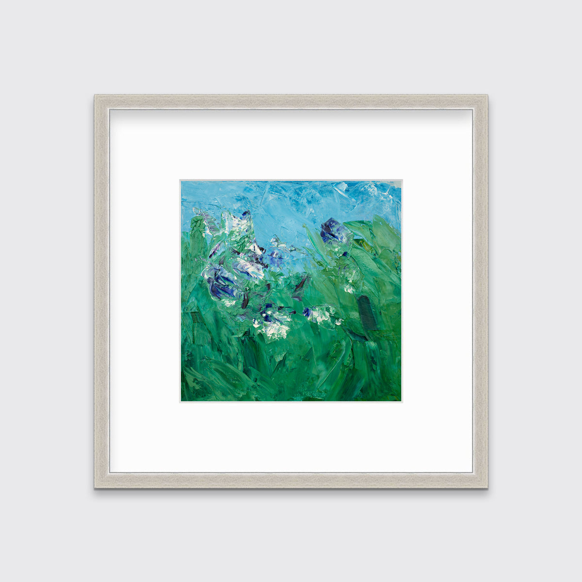 A blue, green, purple and white abstract landscape print in a silver frame with a mat hangs on a white wall.