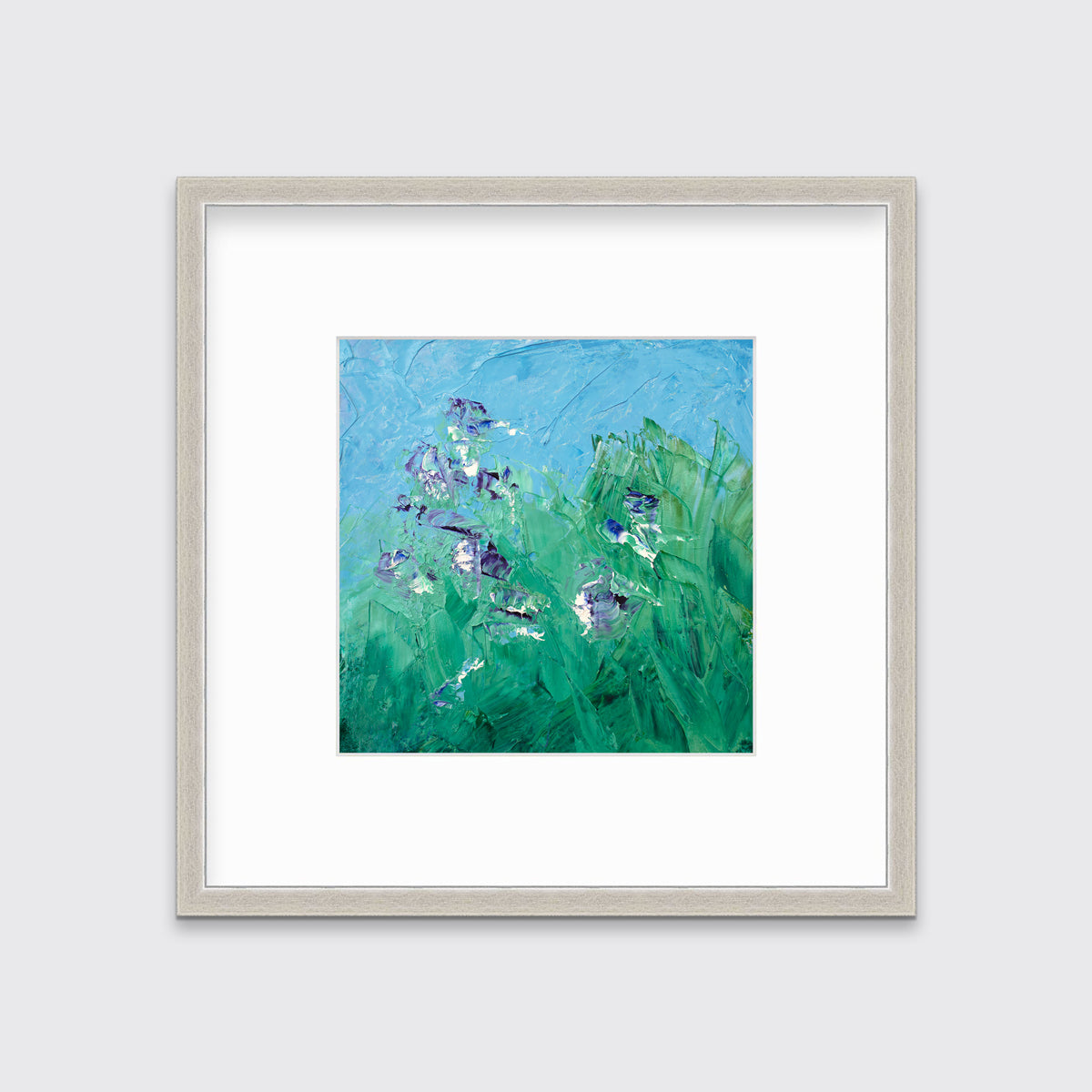 A blue, green, purple and white abstract landscape print in a silver frame with a mat hangs on a white wall.