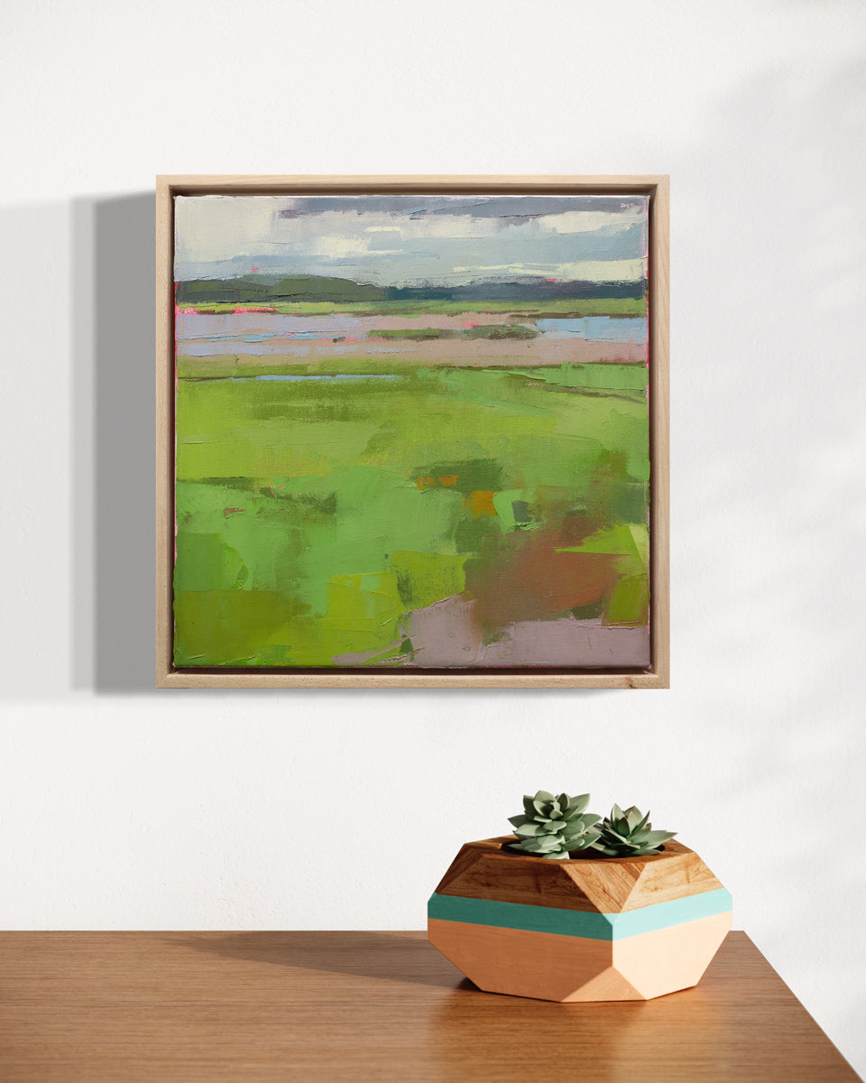 A framed textured abstracted landscape painting hangs on a white wall above a wood table surface, on which rests a geometric wood planter holding succulents.