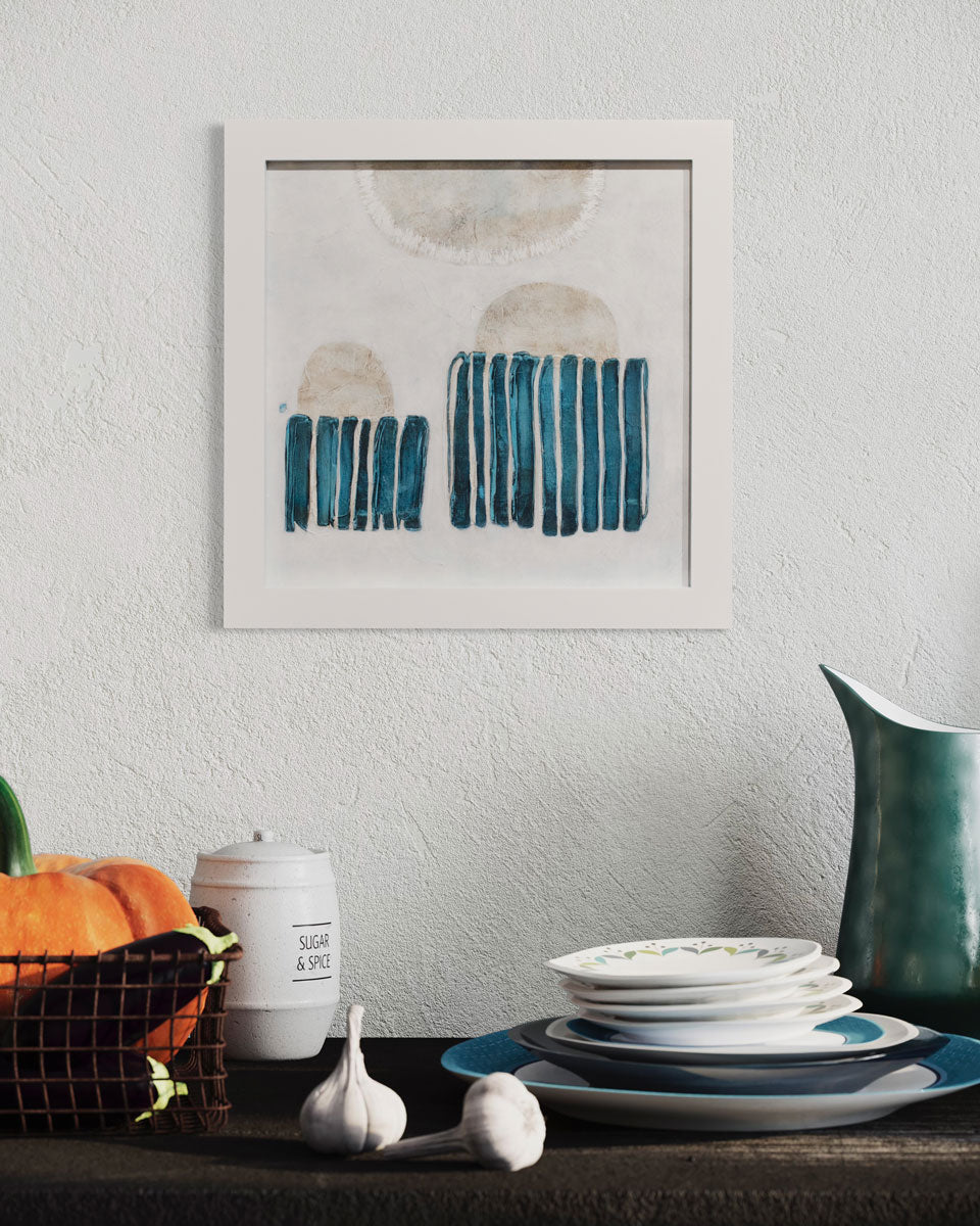 A framed blue and white abstract painting hangs on a textured wall above dishes, a vegetable basket and sugar jar.