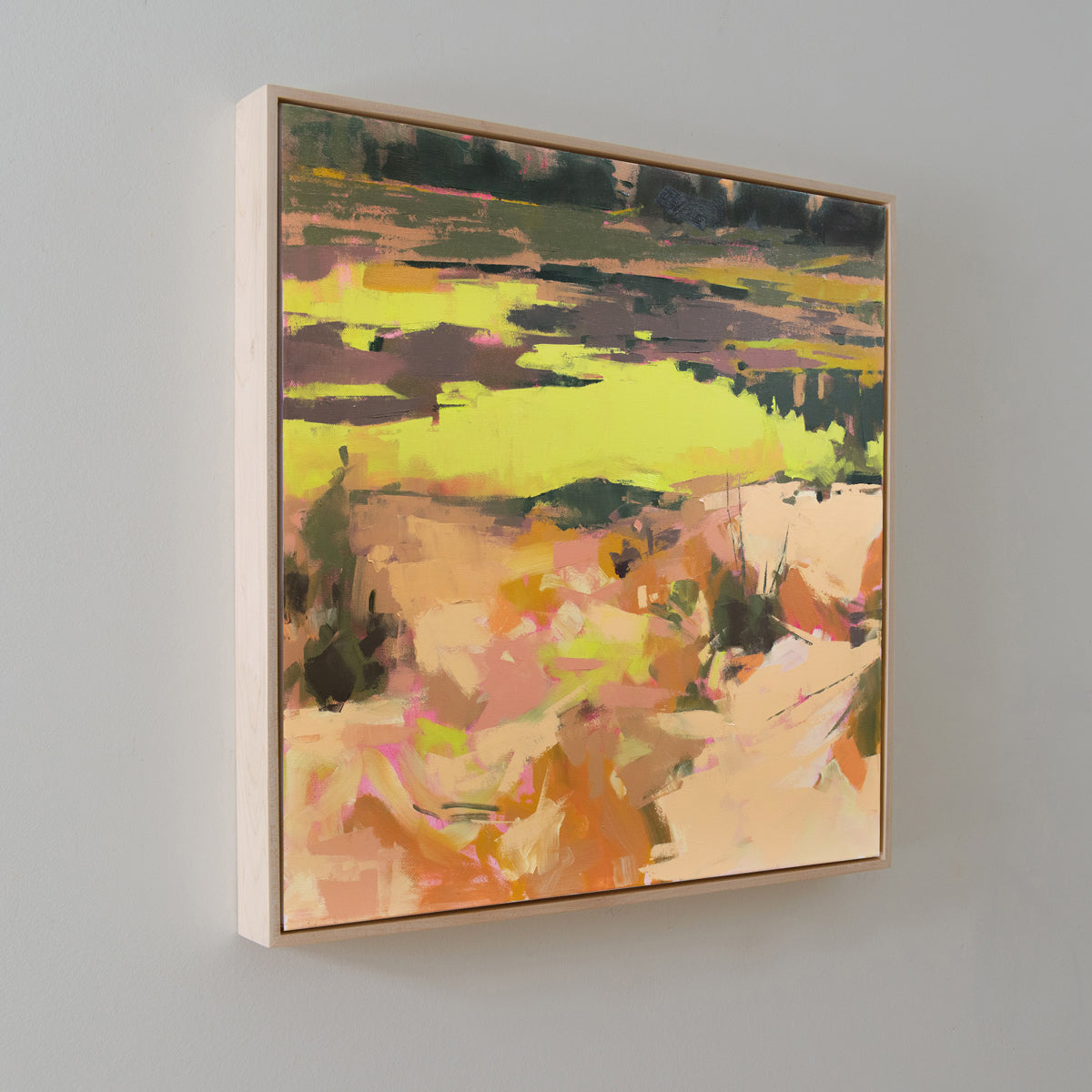 A yellow and orange abstract landscape painting hangs on a white wall on an angle.