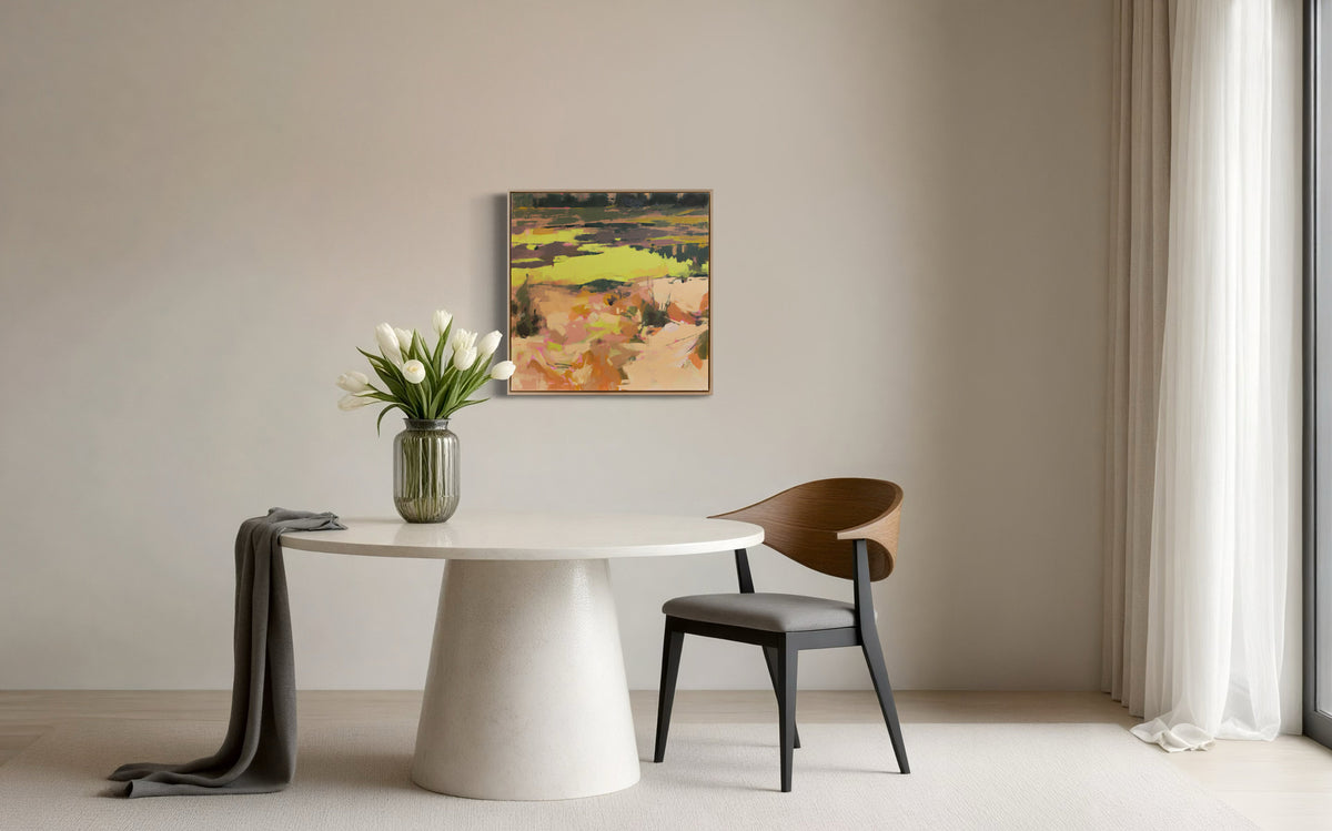 A yellow and orange abstract landscape painting hangs on a white wall over a whit round table. A chair is to the right and a vase of white tulips sits on the table.