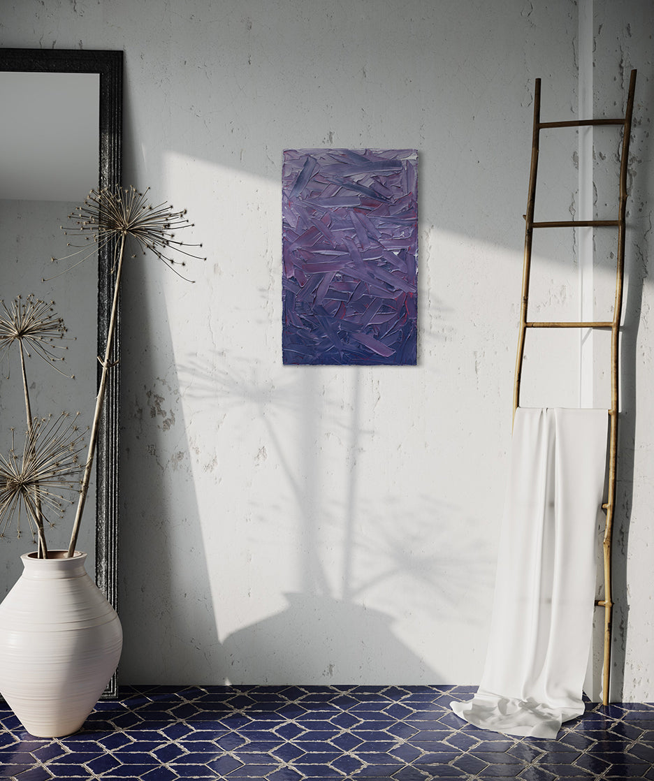 A tonal purple and pink thickly textured abstract painting by Teodora Guererra hangs on a white wall. To the right is a natural wood decorative ladder with a white fabric draped over it. to the left is a wall mirror with a dark ridged frame leaning on the wall and a large white ceramic pot with decorative sticks in front. The floor below is a dark blue tile in a geometric pattern with grey grout.