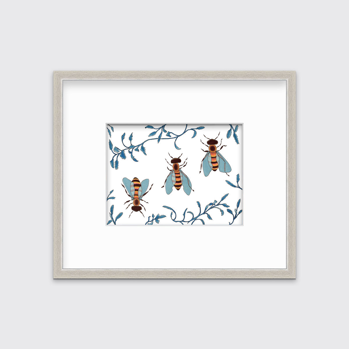 A print of three bees surrounded by blue ferns in a silver frame with a mat.