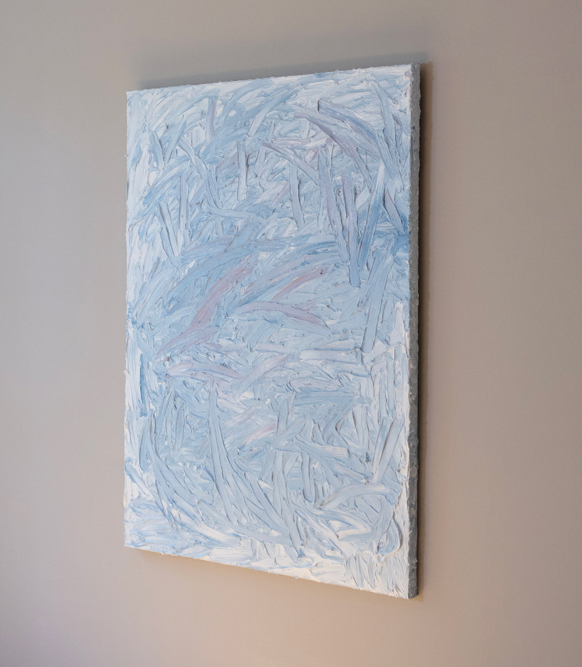 A blue and white textured painting hangs from a side view on a grey wall in the artists studio.