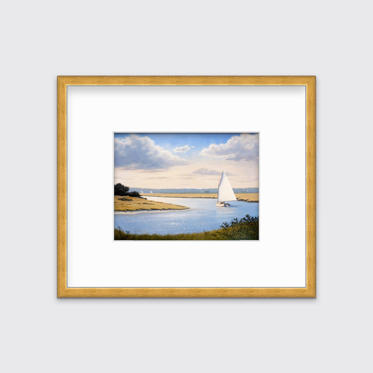 A print of a sailboat going down a winding blue river in a gold frame and mat hangs on a white wall.