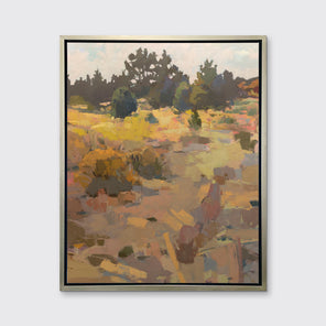 An earth-toned abstracted landscape art print framed in a silver frame hangs on a white wall. 