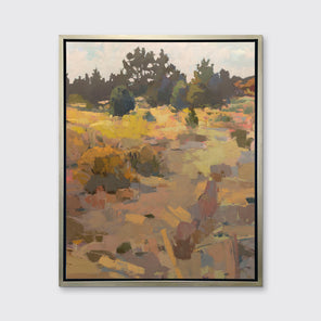 An earth-toned abstracted landscape art print framed in a silver frame hangs on a white wall.