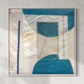 A framed abstract artwork featuring geometric shapes in blue and beige tones with visible stitching and upcycled materials.