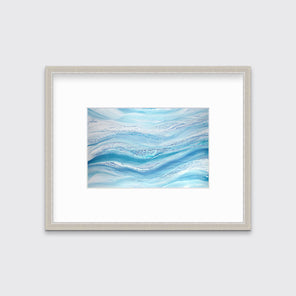 A blue, teal and white abstract print in a silver frame with a mat hangs on a white wall.