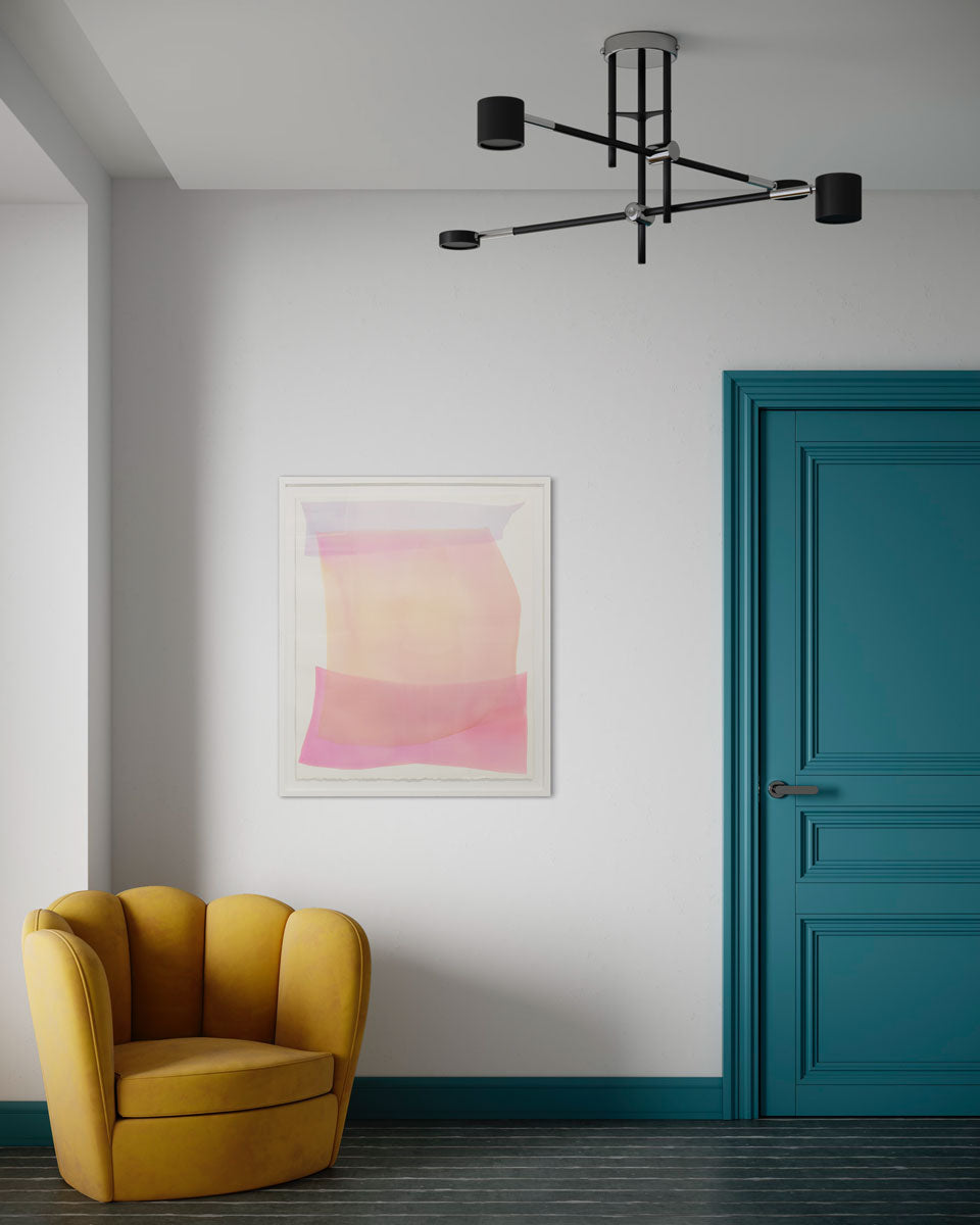 An abstract pink, orange, and lavender painting framed in a white frame, hangs one a white wall above a mustard yellow armchair and next to a deep teal door.