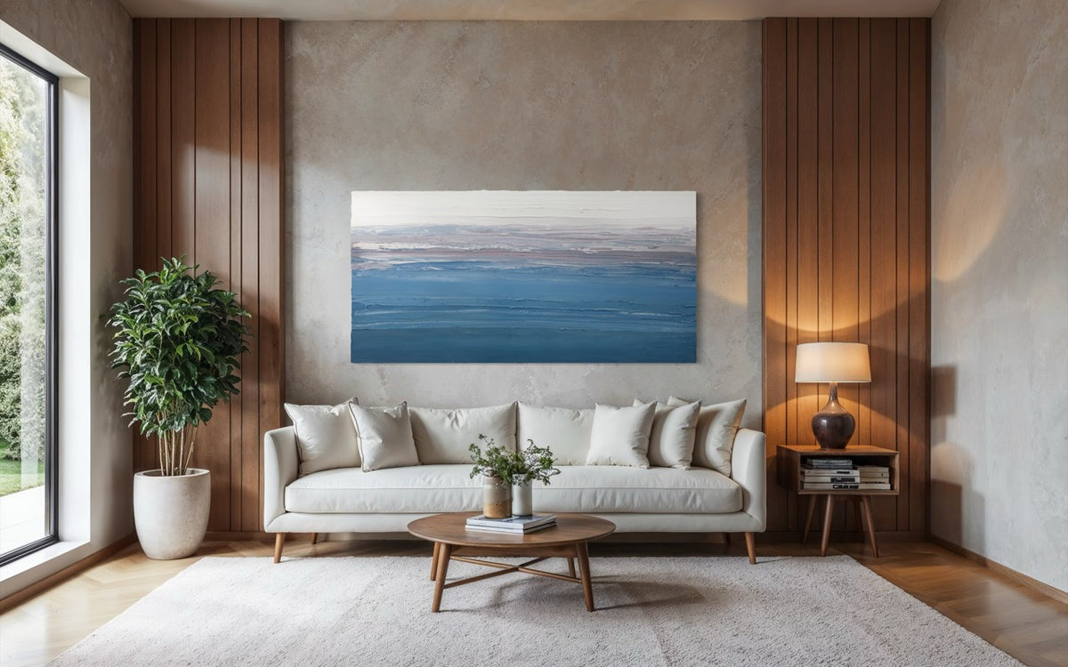 Modern living room with an original abstract painting by Teodora 'teo' Guererra depicting textured horizontal lines in varying shades of blue and white over a white sofa, and decorative elements.