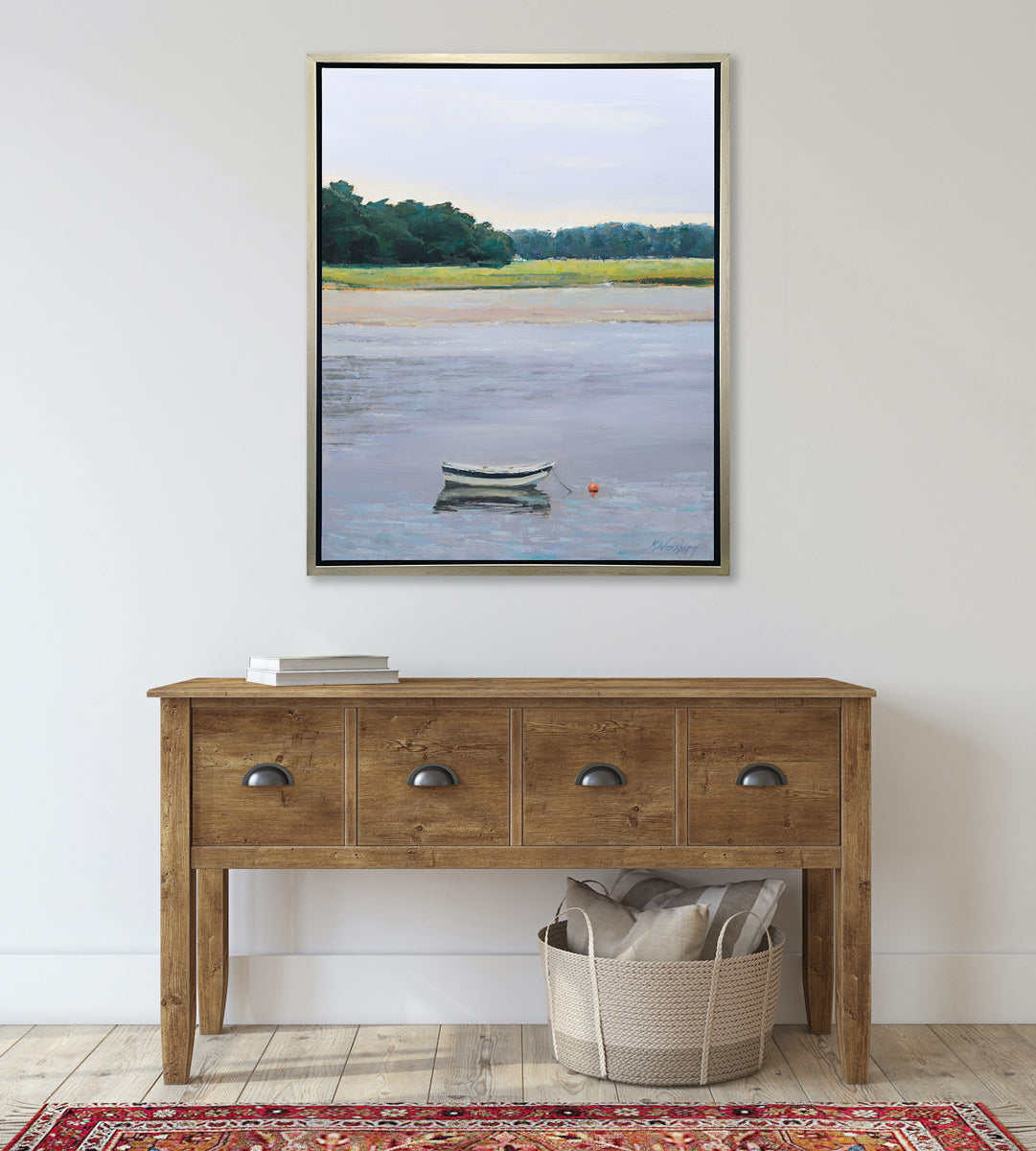 A limited edition landscape print framed in a silver frame hangs on a white wall above a wood console table and red carpet.