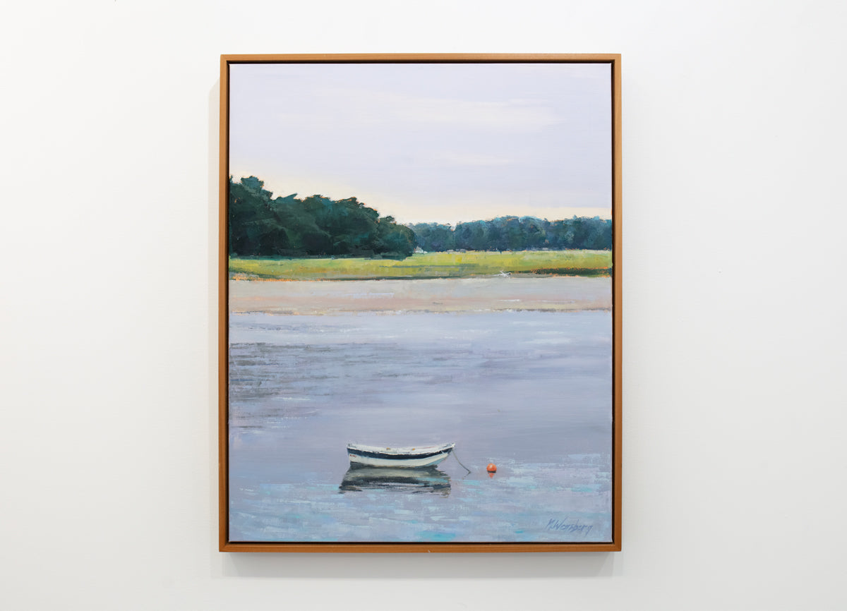A light coastal landscape painting framed in a light wood frame hangs on a white wall.