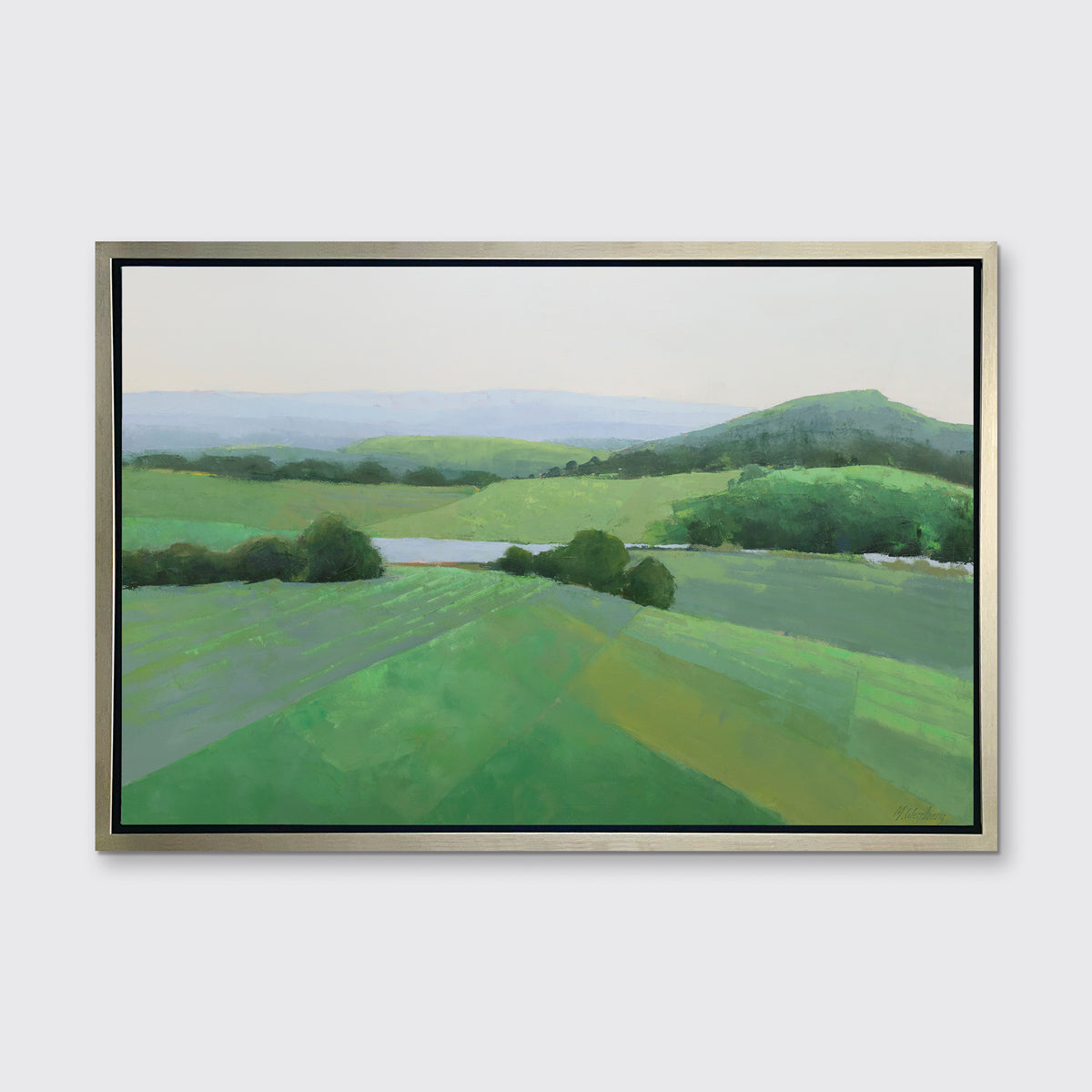 A green landscape art print framed in a warm silver frame hangs on a white wall.
