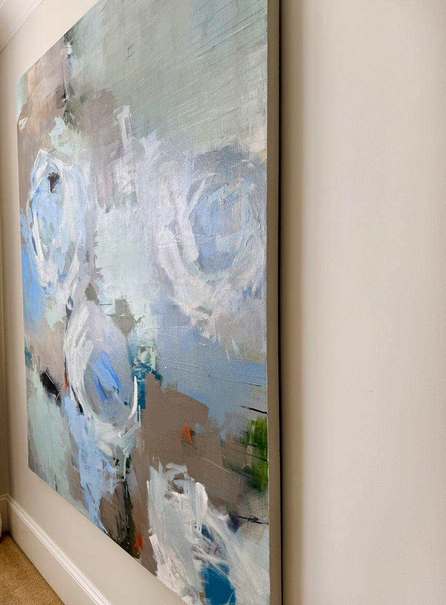 Abstract painting, side view, with blue and white tones on a beige wall.