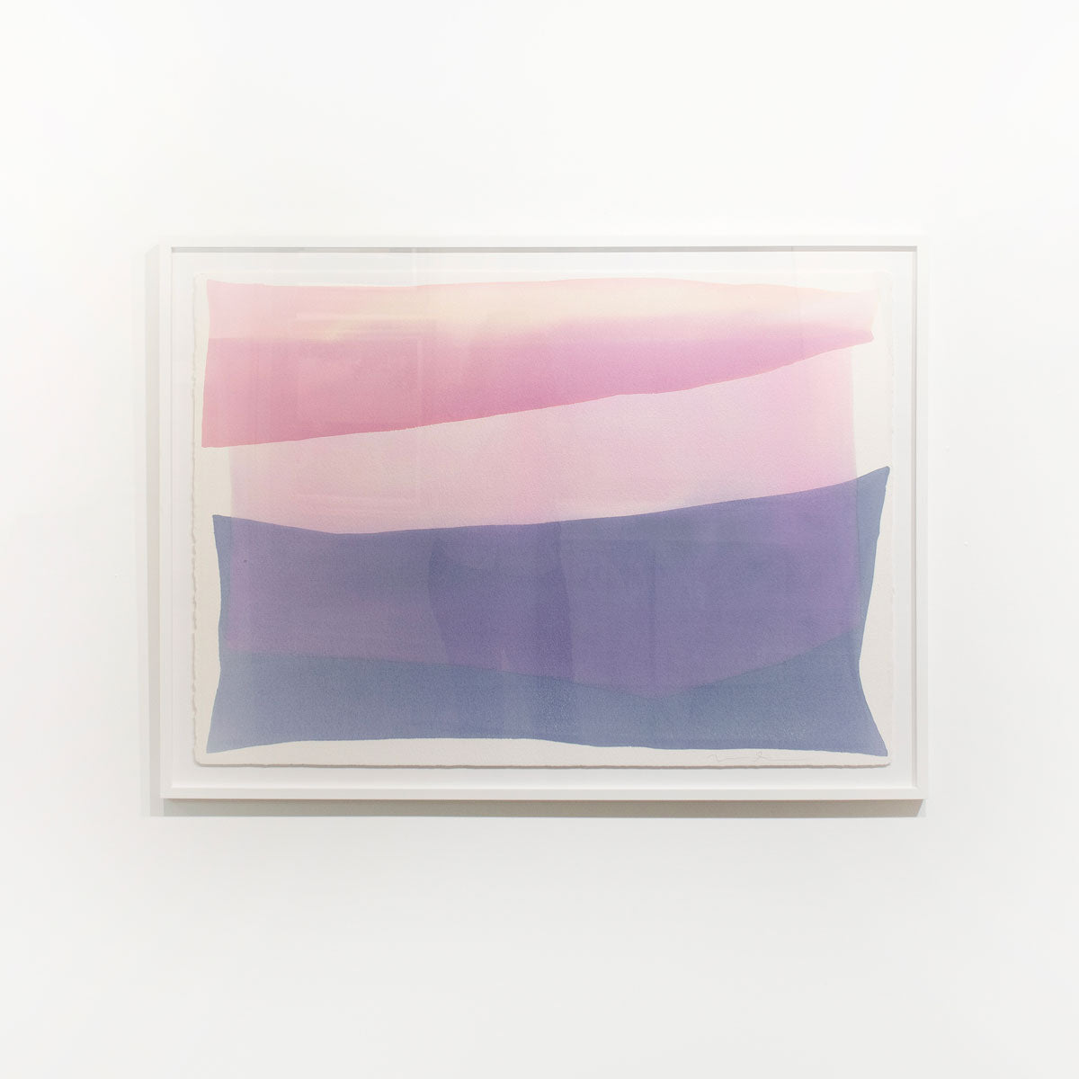 A pink and violet abstract watercolor painting framed in a white frame hangs on a white wall.
