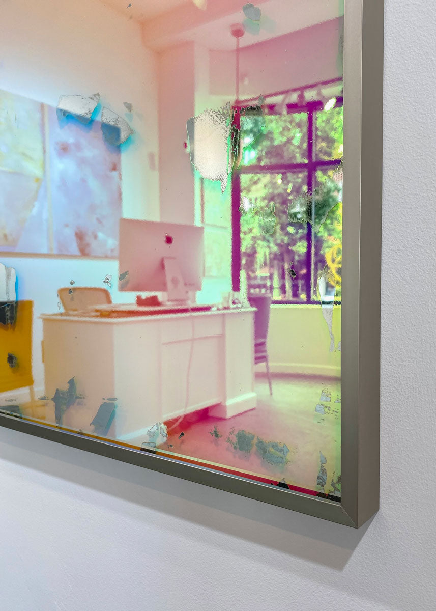 A detail of the corner of a framed fine art mirror hanging on a white wall.