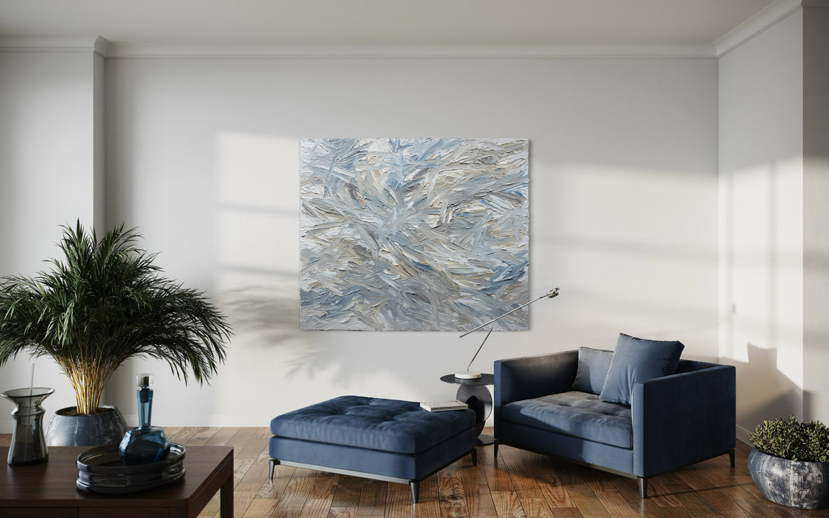 Modern living room with a blue sofa, ottoman, and an original abstract painting by Teodora Guererra, hanging on a white wall.