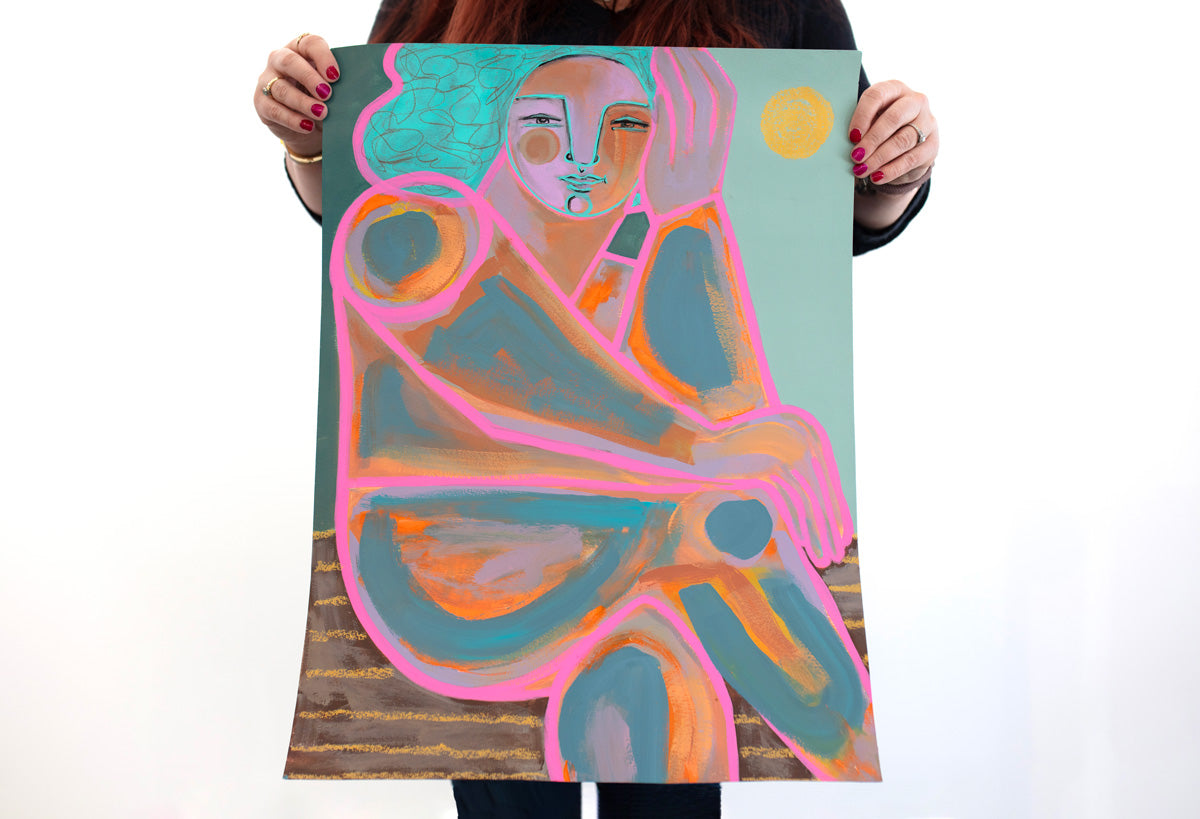 A woman holds a pink, yellow, orange, and turquoise abstract painting on paper of a woman in front of a white wall.