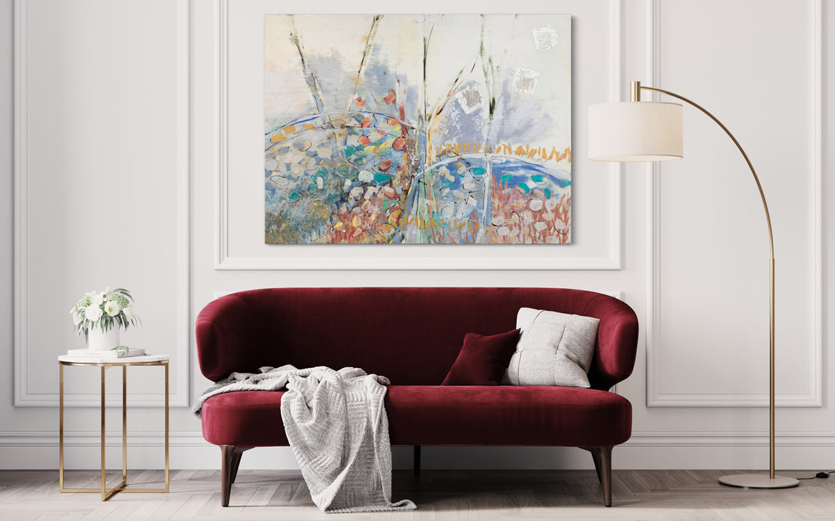 A multicolored abstract painting hangs on a white wall above a modern red suede sofa with a white pillow and throw, and a gold floor lamp on one side and a modern gold end table on the other.