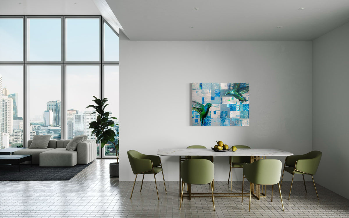 An abstract painting of two humming birds, hangs on a light grey wall, over a dining table.