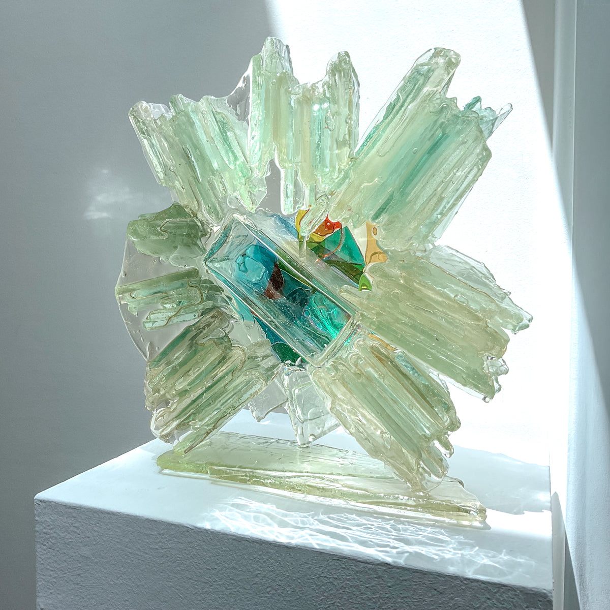 An abstract glass sculpture on a white pedestal against a neutral background.