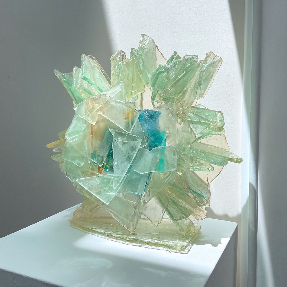 An abstract glass sculpture on a white pedestal against a neutral background.