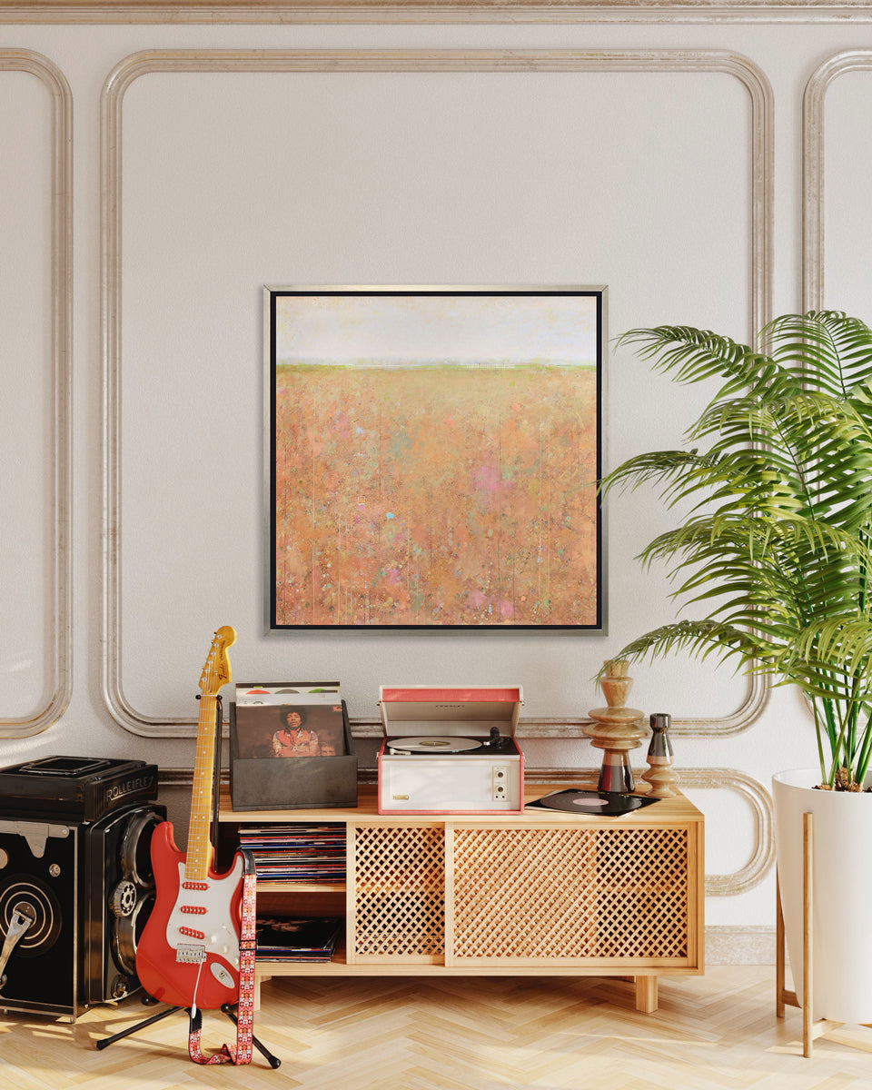 A orange, light green, light blue and pink abstract landscape print in a silver floater frame hangs on a white inset wall above a natural wood credenza with a record player, stacks of records and a red and white guitar in front.