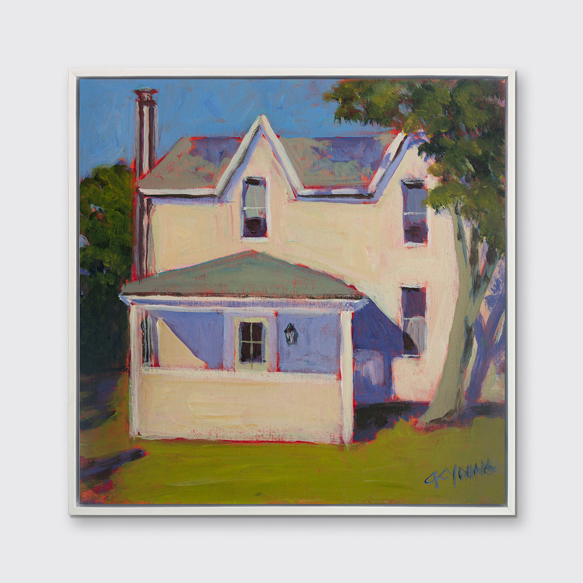 A print of a white house that sits next to a giant tree, green grass in front in a white floater frame hangs on a white wall.