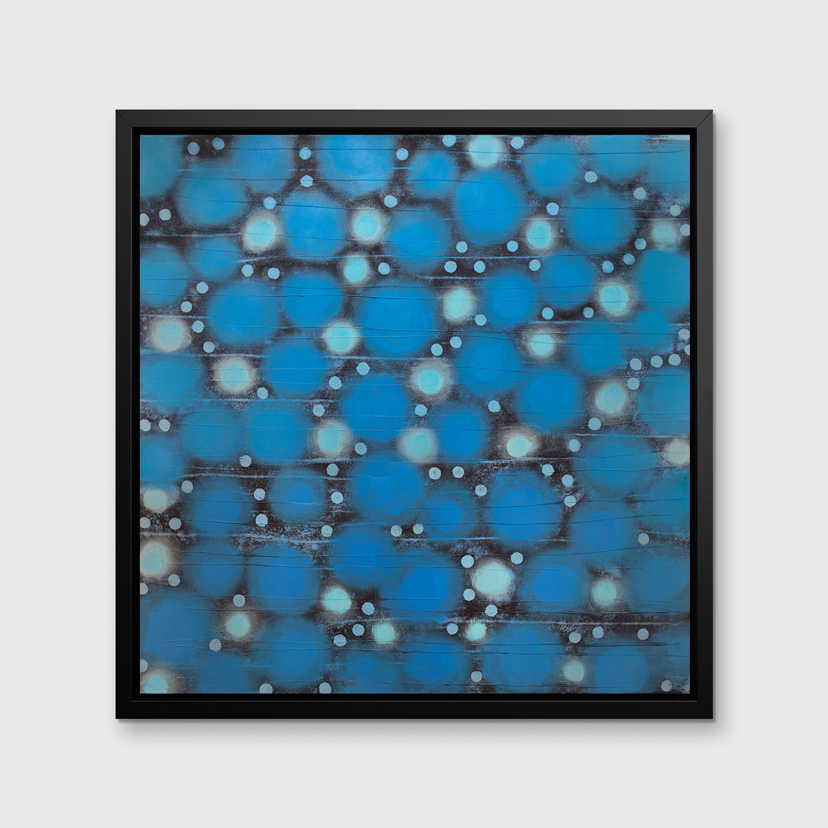 A blue, teal and black abstract circle print in a black floater frame hangs on a white wall.