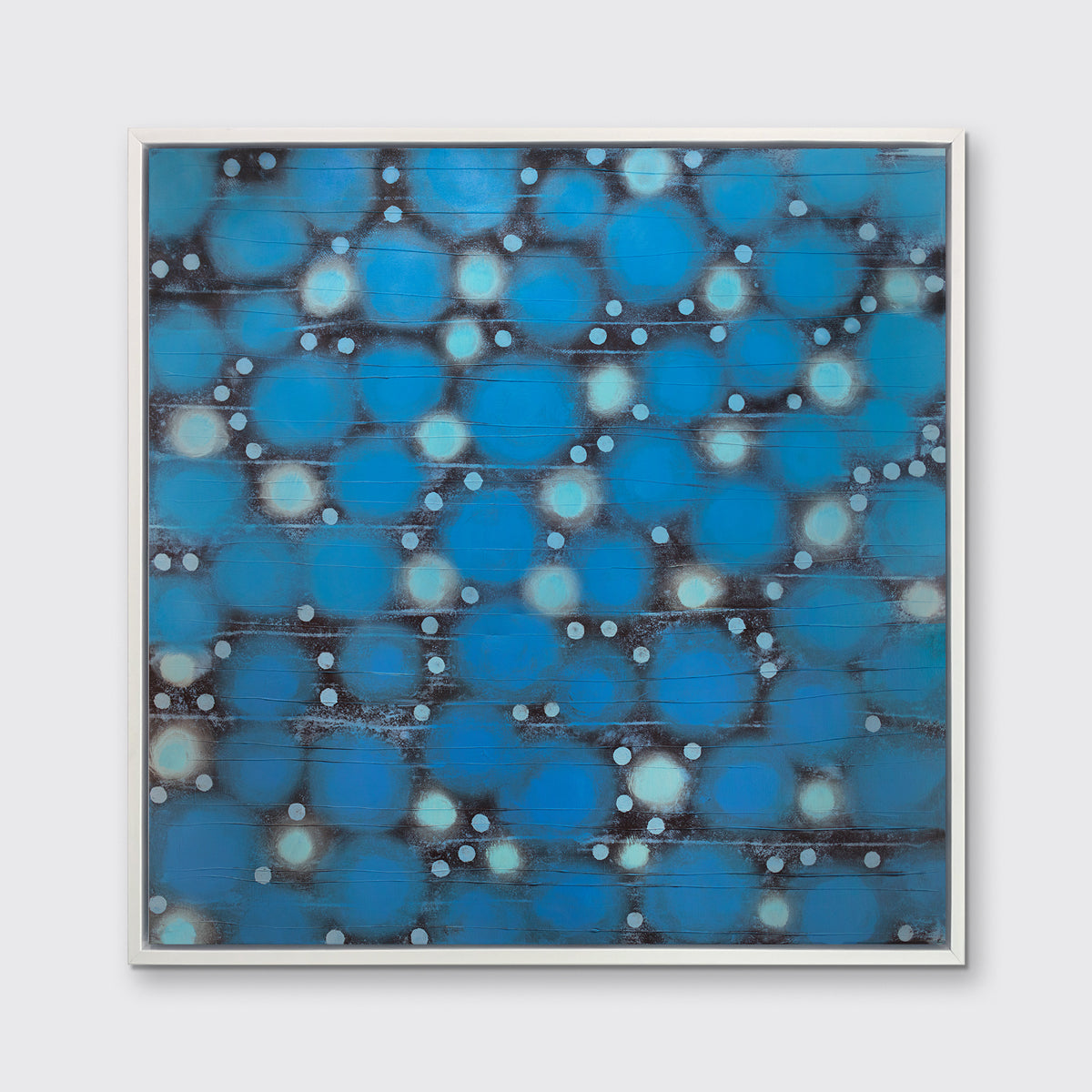 A blue, teal and black abstract circle print in a white floater frame hangs on a white wall.