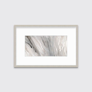 A beige, white and gold abstract print in a silver frame with a mat hangs on a white wall.