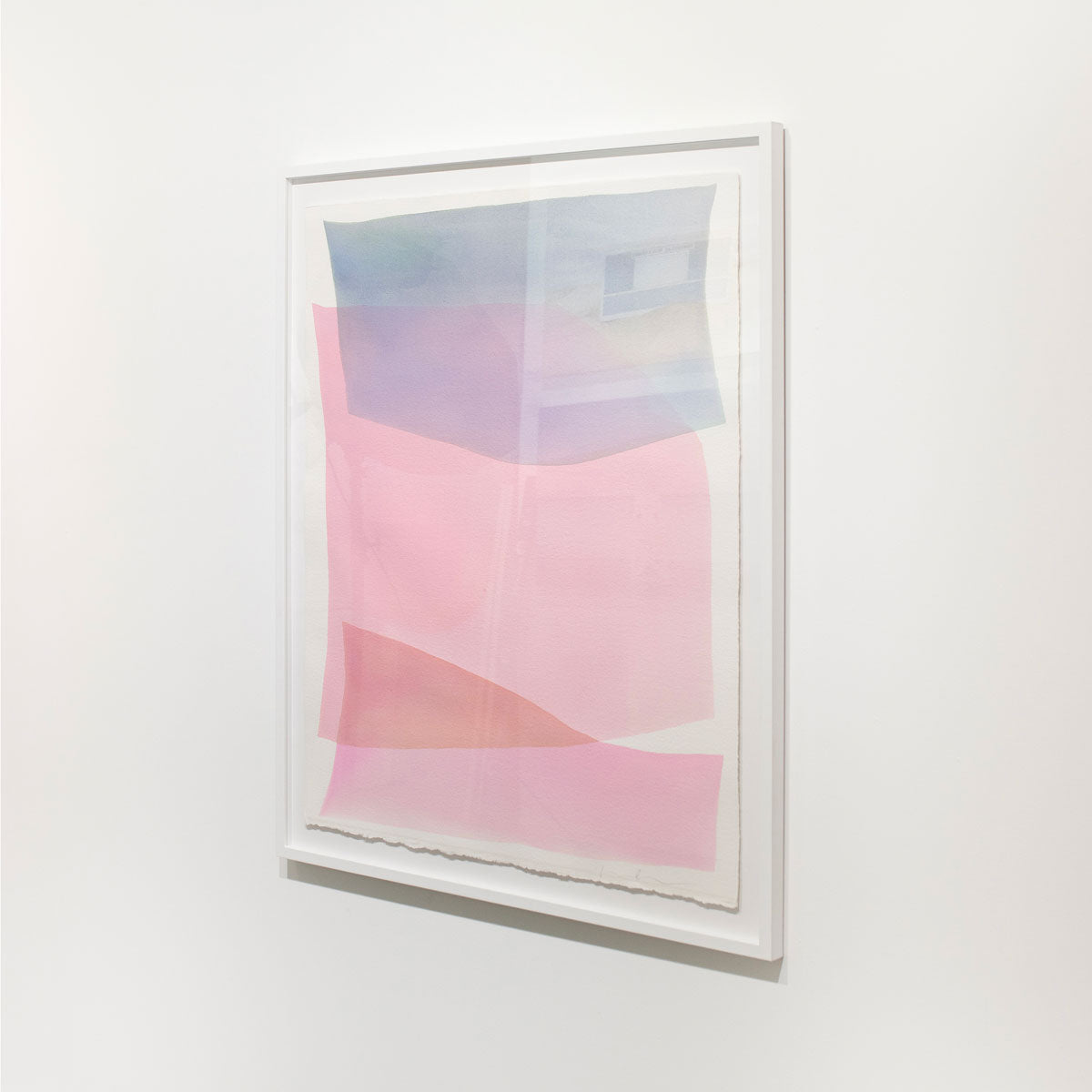 A framed pink and light blue abstract watercolor painting hangs on a white wall.