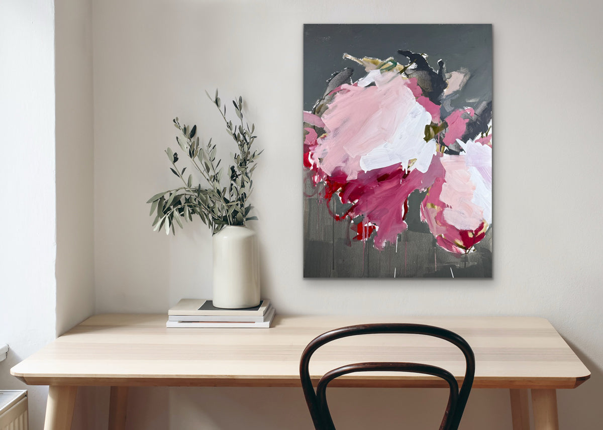 Floral painting on a wall above a wooden table with a vase and books.