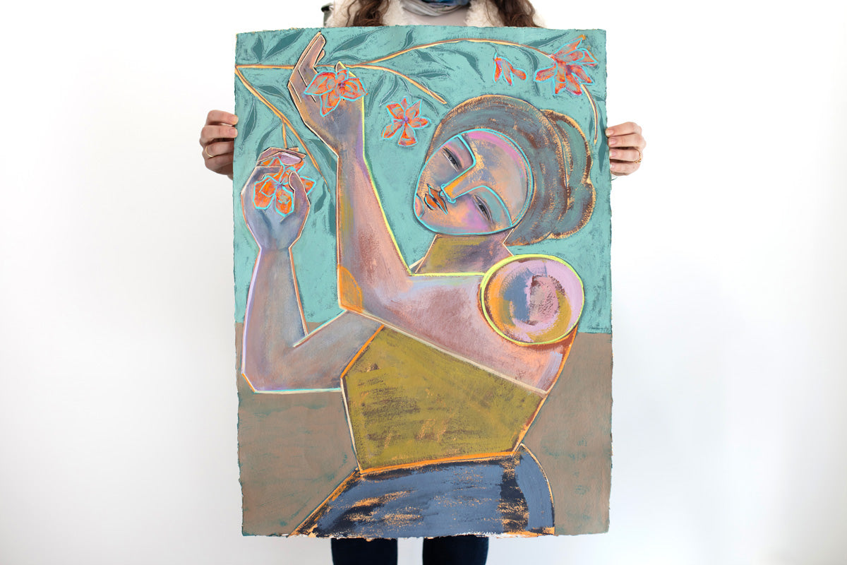 A woman stands in front of a white wall holding an abstracted blue, turquoise and yellow painting of a woman holding flowers from a branch on paper.