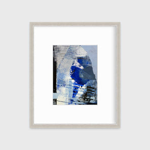 A blue, white and black abstract print in a silver frame with a mat hangs on a white wall.