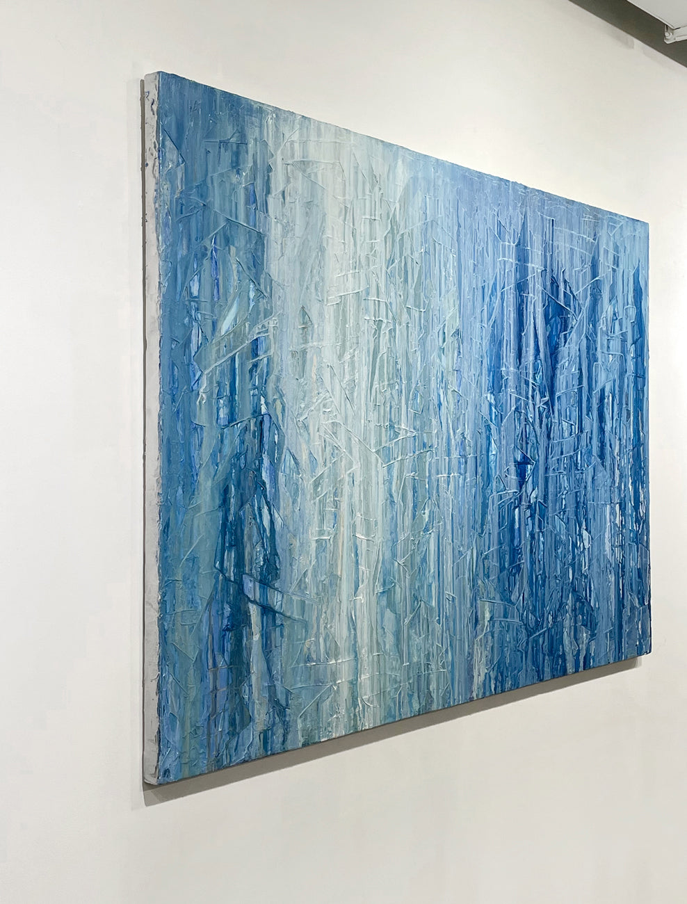 An Original abstract blue and white painting on a white wall by Teo Guererra, side view.