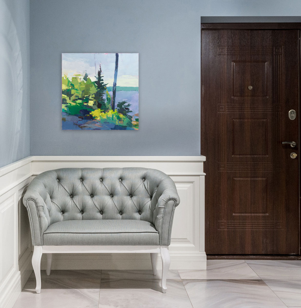 An abstracted landscape painting hangs above a modern grey armchair on a light grey wall.
