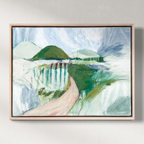 Framed painting of a landscape with mountains and a waterfall on a white wall.