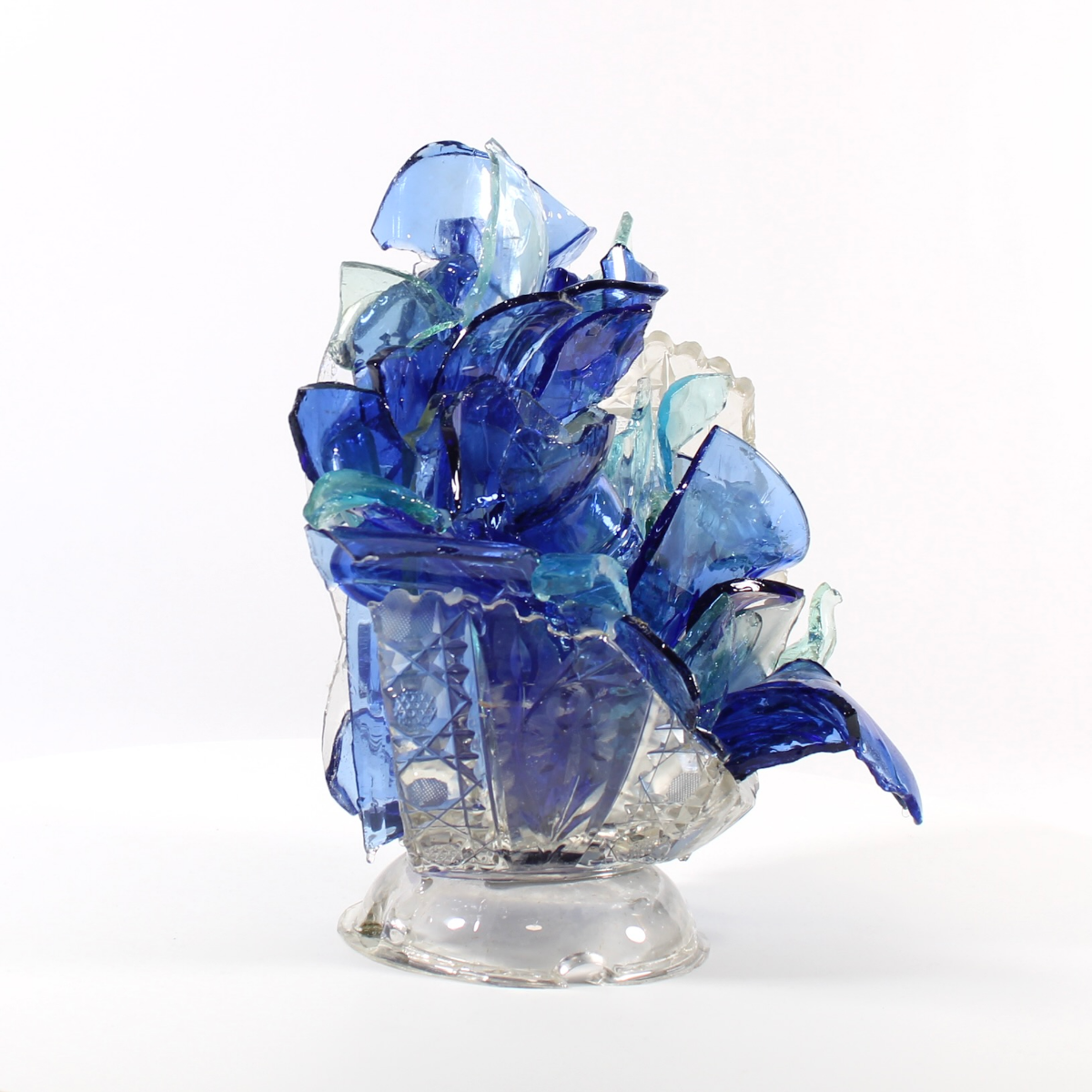 Glass sculpture of blue flowers in a clear vase on a white background.