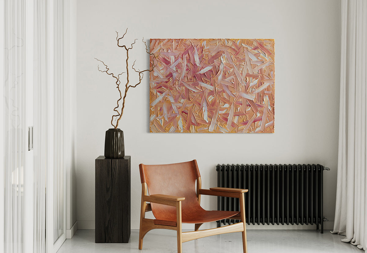 A orange, pink, coral and white thickly textured abstract painting hangs on a white wall above a black radiator. To the left is a dark wood pedestal with a black ceramic pot and decorative sticks and in front is a cognac leather contemporary directors type chair.