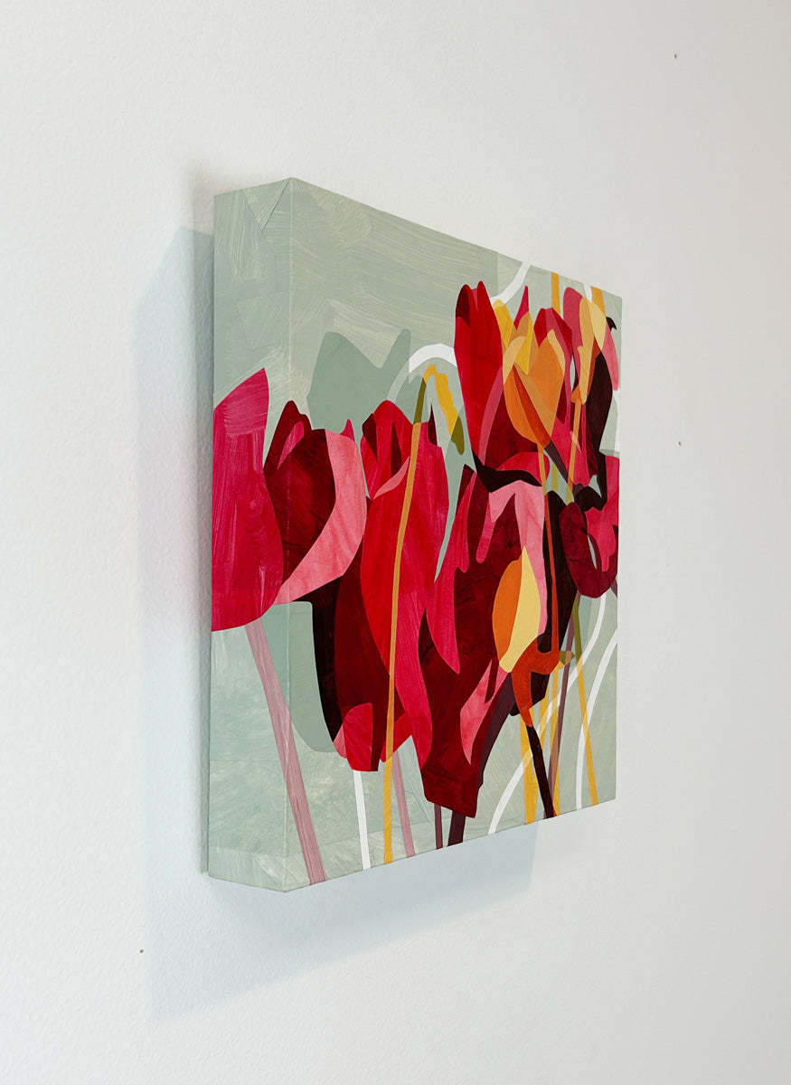 A colorful abstract floral artwork on a wall, featuring predominantly red and pink tones with touches of yellow and green hanging on a white wall, side view.
